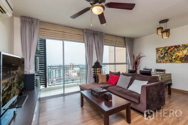 Condominium for rent in Bang Na, Bangkok - Living area with floor‑to‑ceiling windows opening to a balcony and dining space.
