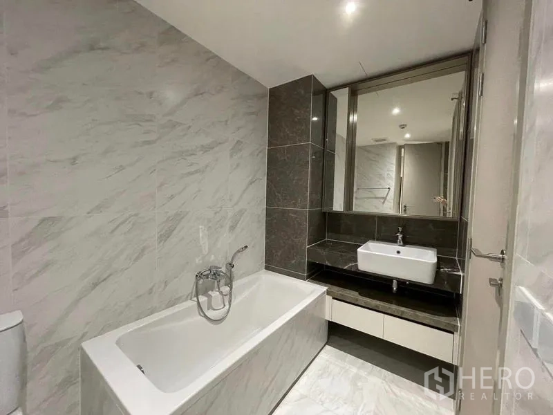 Condominium for rent in Khlong Toei, Bangkok - Modern bathroom with marble tiles, bathtub and vanity with mirror