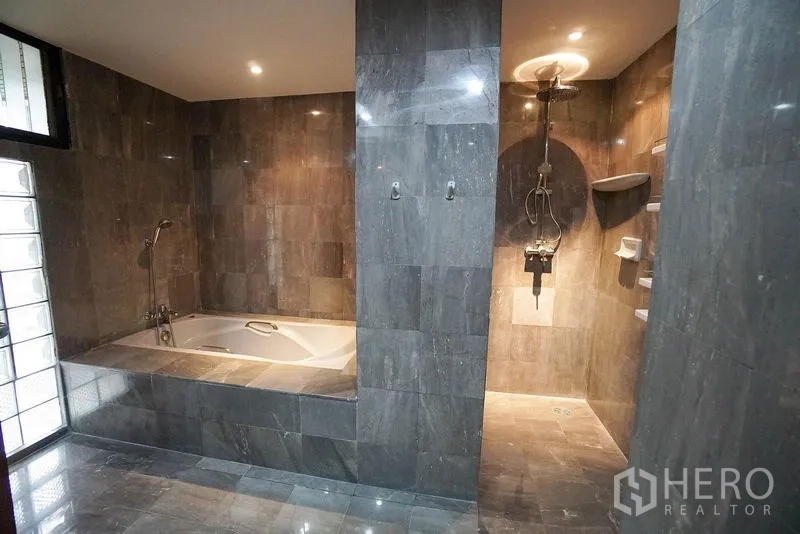 Apartment for rent in Watthana, Bangkok - Ensuite bathroom with a deep soaking tub and separate walk-in rain shower clad in gray tiles.