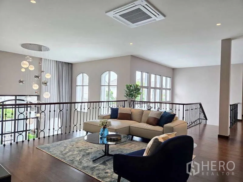 Detached House for rent or sale in Lat Krabang, Bangkok - Open mezzanine family lounge with sectional sofa, railing, and expansive windows.