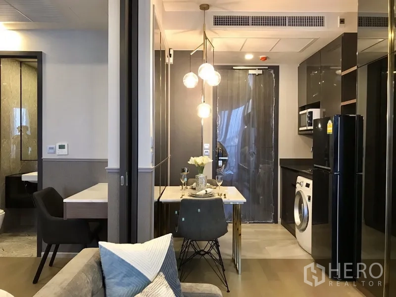 Condominium for rent in Watthana, Bangkok - Compact kitchen with glossy cabinets, washing machine and a two-seat dining nook under pendant lights in a modern condo.