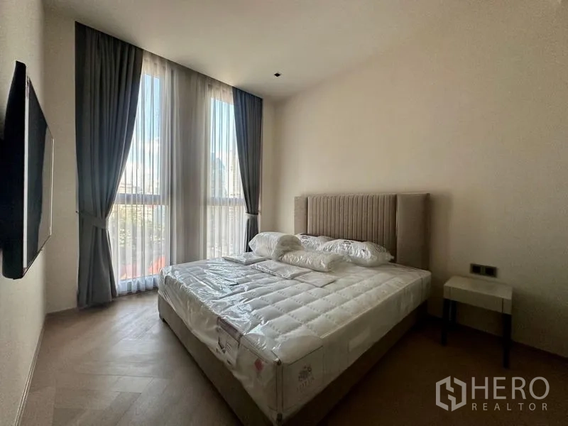 Condominium for rent - Bright bedroom with upholstered headboard, large windows and wall-mounted TV.