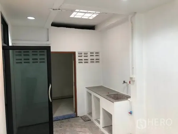 Townhouse for rent in Watthana, Bangkok - Simple kitchen and utility zone with concrete countertop, sink and a sliding glass door in a bright white room.