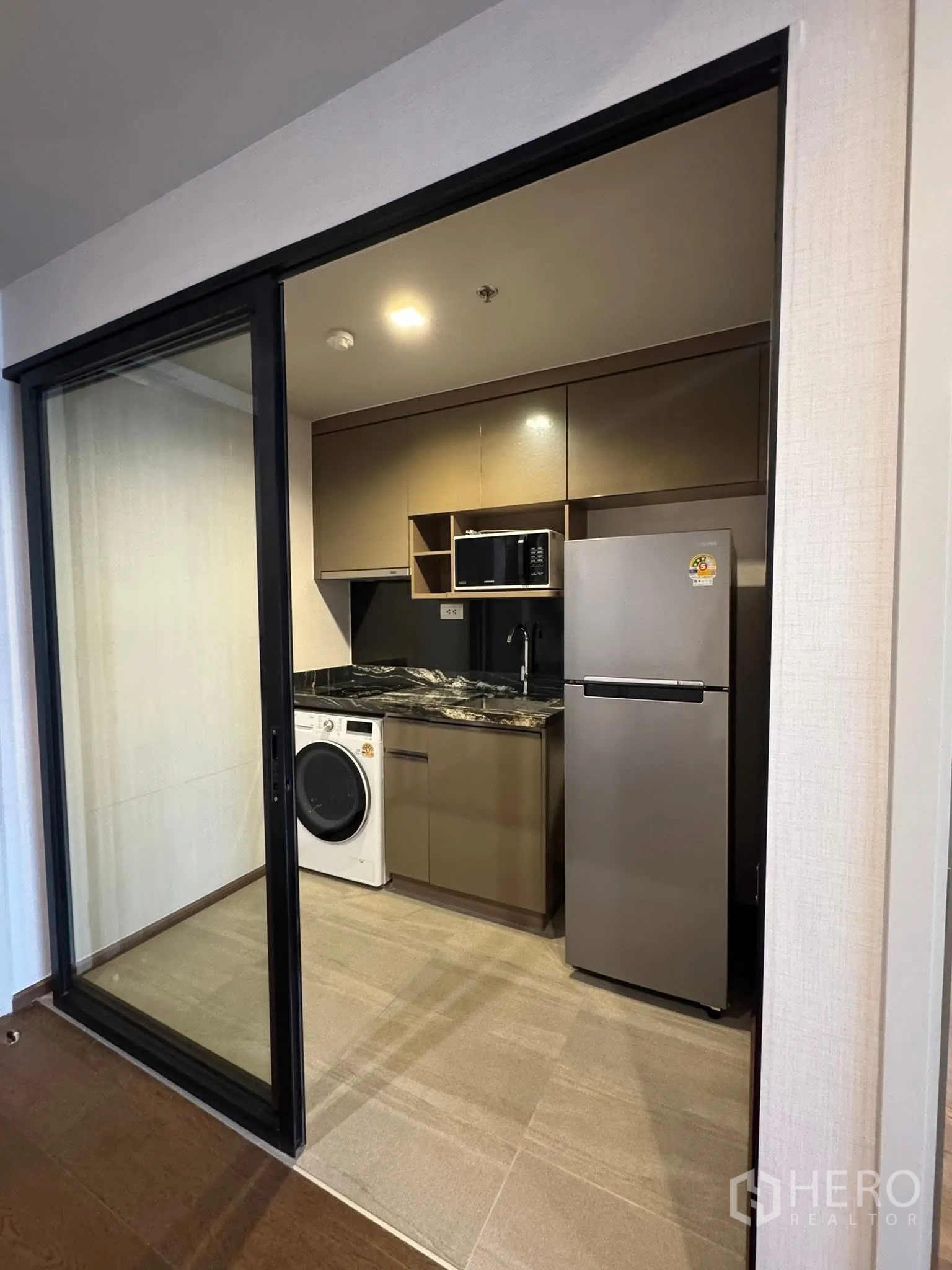 Condominium for rent in Khlong Toei, Bangkok - Enclosed kitchen with fridge, microwave, washer and dark stone countertop.