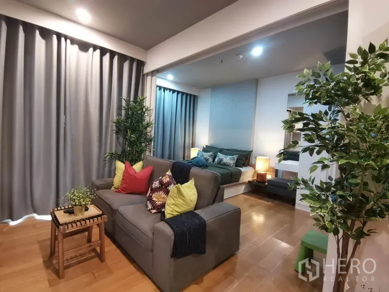 公寓 出租或出售在Watthana, Bangkok - 起居区与卧室相连，灰色窗帘与彩色抱枕沙发。
