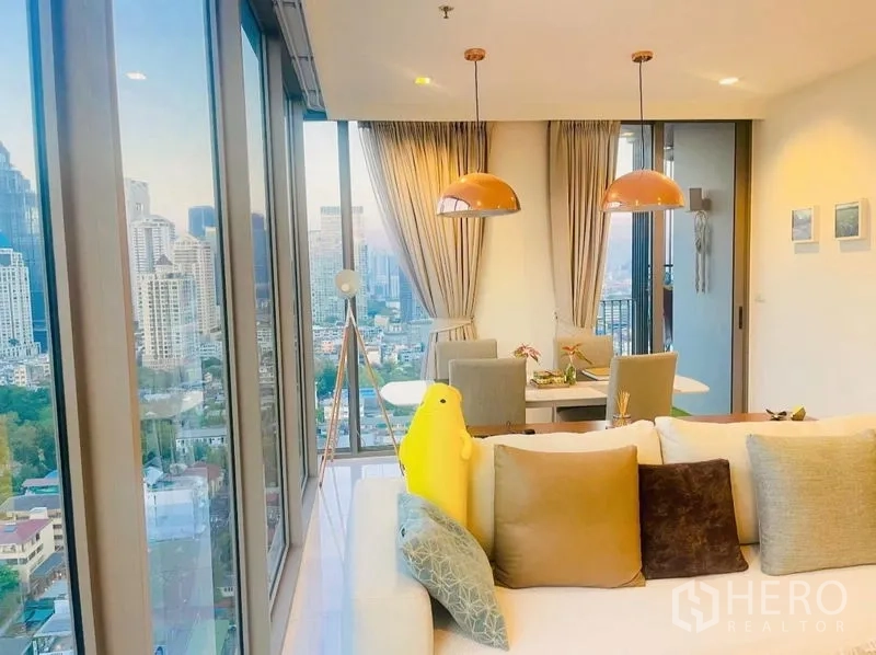 Condominium for rent or sale in Sathon, Bangkok - Sofa facing dining zone and balcony framed by tall glass walls.