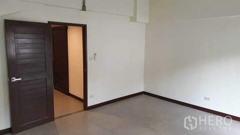 联排别墅 出租或出售在Khlong Toei, Bangkok - 宽敞卧室，木门与中性色瓷砖地面。