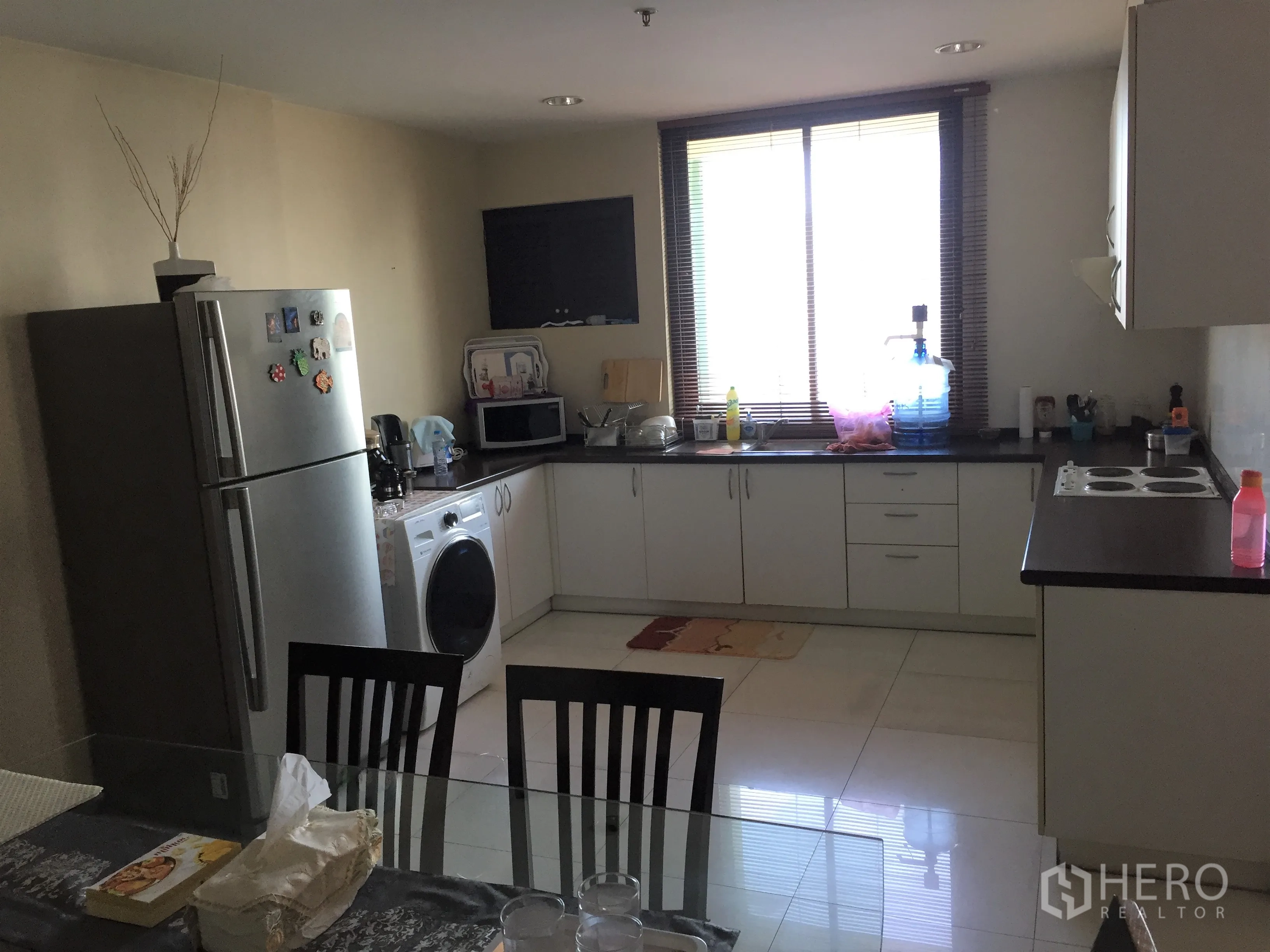 公寓 出租或出售在Khlong Toei, Bangkok - 采光良好的厨房，白色橱柜、窗户、冰箱、洗衣机与餐桌，功能齐全。