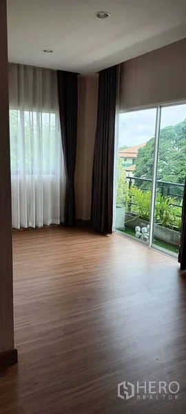 Townhouse for rent or sale in Saphan Sung, Bangkok - Corner bedroom with curtains and sliding glass door opening to a balcony.