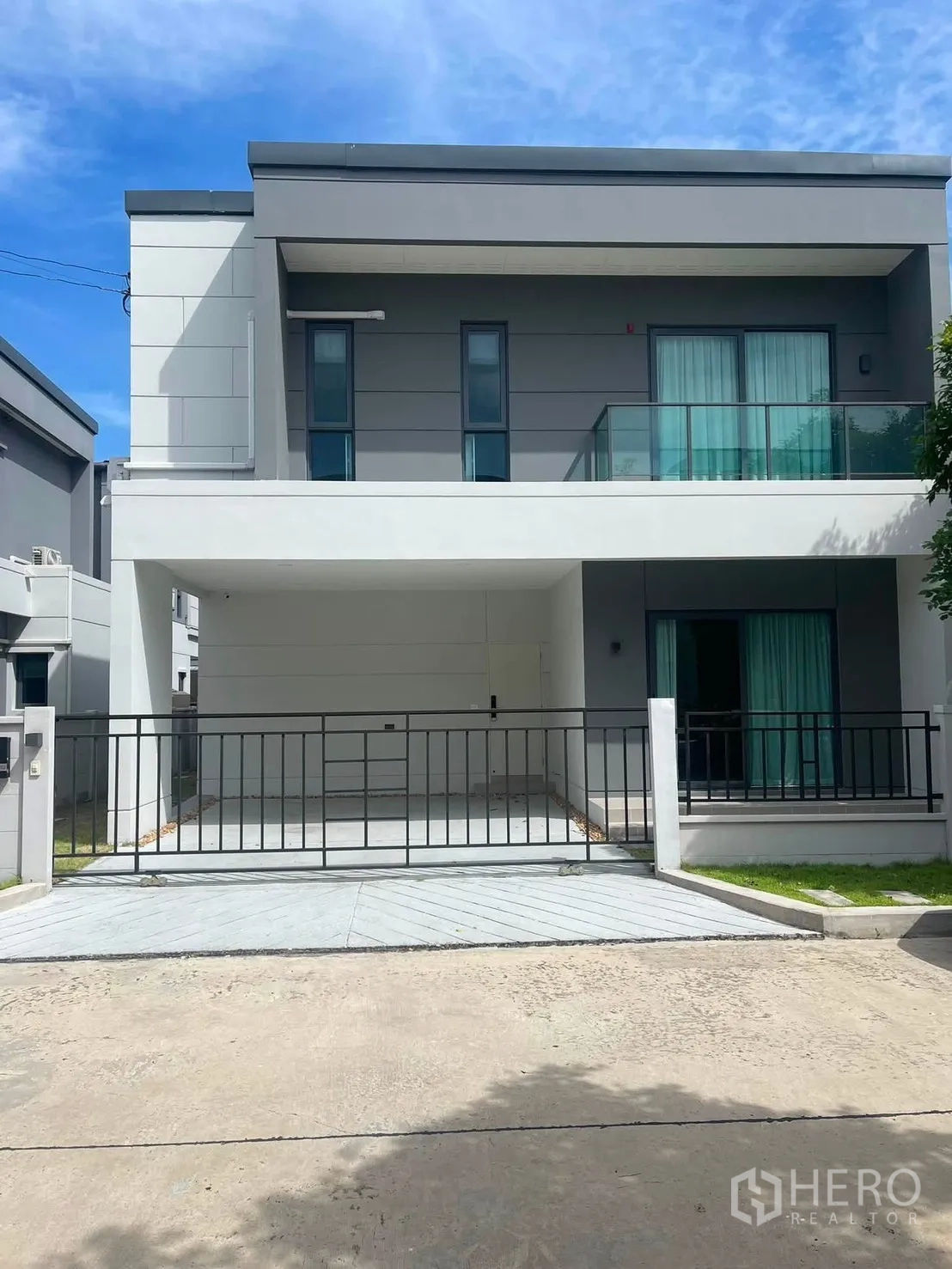 Detached House for rent in Bang Phli, Samut Prakan - Modern two-storey house facade with a balcony, sliding gate, driveway, and small lawns.