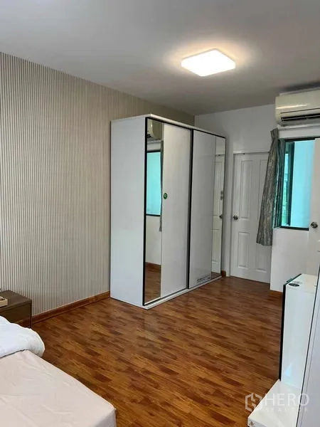 Townhouse for rent in Phra Khanong, Bangkok - Spacious bedroom with wood flooring, sliding wardrobe, air conditioner and window.