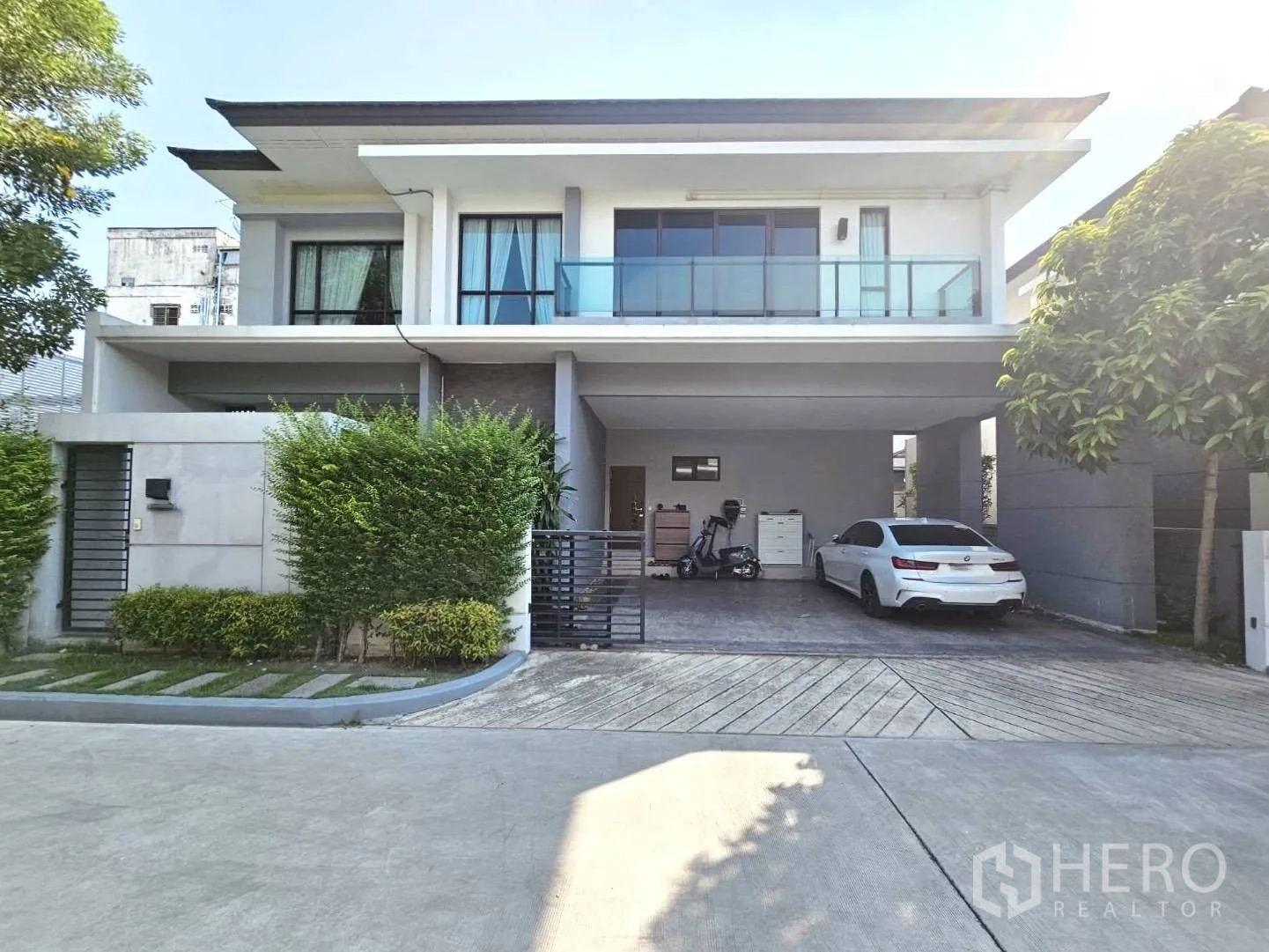 บ้านเดี่ยว for rent in Wang Thonglang, Bangkok - บ้านสองชั้นสมัยใหม่พร้อมรั้ว หน้าบ้านมีที่จอดรถในร่มสองคัน ระเบียงและทางรถเข้า.