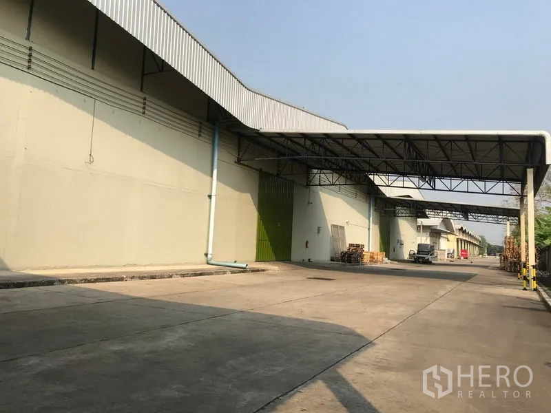 Warehouse for rent in Bang Pa-in, Phra Nakhon Si Ayutthaya - Large warehouse exterior with covered loading bays and a wide concrete driveway for trucks in Bang Pa-in.