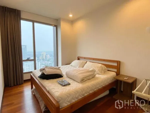 Condominium for rent - Bedroom with large window, wooden bed frame and skyline view, featuring soft recessed lighting.