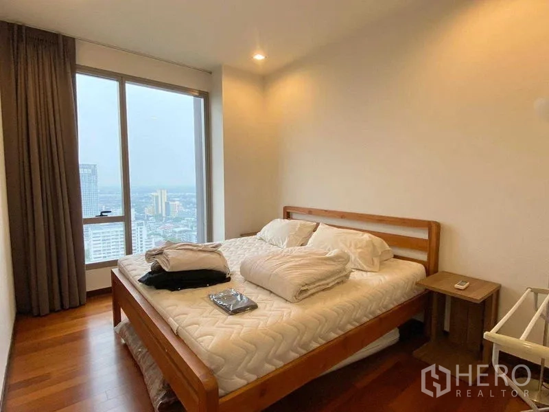 Condominium for rent - Bedroom with large window, wooden bed frame and skyline view, featuring soft recessed lighting.
