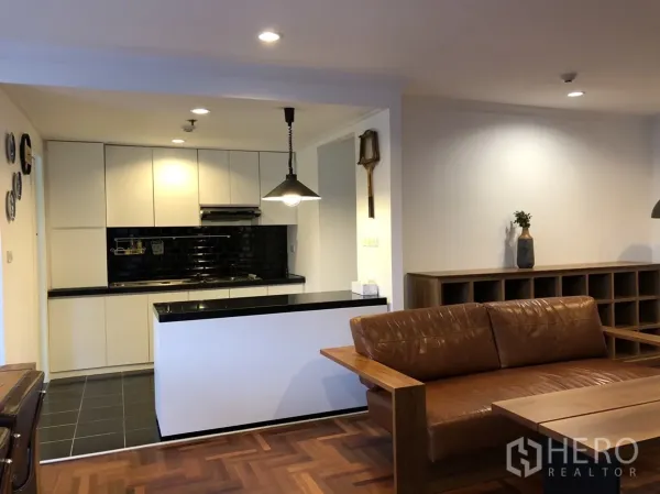 公寓 出租在Watthana, Bangkok - 开放式客厅与厨房，棕色皮沙发、木地板与黑色地铁砖背景墙