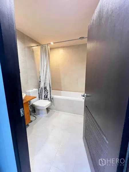 公寓 出租在Ratchathewi, Bangkok - 从门口看到的浴室，浴缸带浴帘与木质洗手台。