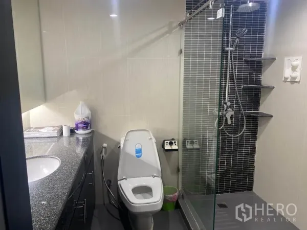 Condominium for rent in Khlong Toei, Bangkok - Bathroom with glass-enclosed shower, rainfall head, mosaic tile wall, and toilet.