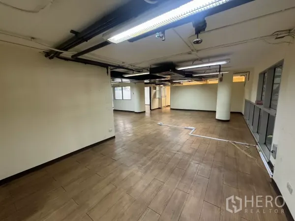 Warehouse for rent - Open‑plan air‑conditioned warehouse office with wood‑look tile flooring, exposed ducts, pillars and fluorescent lighting.