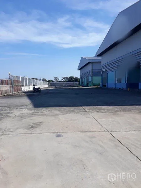 Factory for rent in Samut Prakan - Expansive paved yard in front of the warehouse with fenced perimeter for trucks.