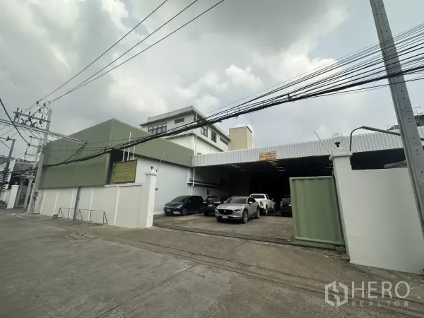 Warehouse for rent in Yan Nawa, Bangkok - Street view of a gated warehouse complex in Yan Nawa with green metal cladding and front parking.