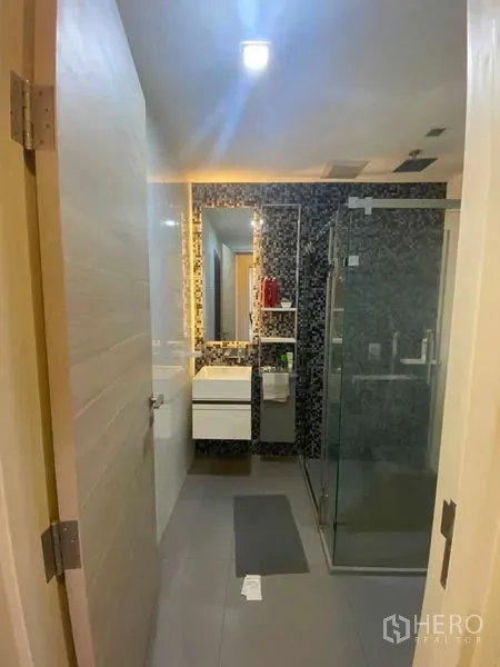 Condominium for rent or sale in Bang Rak, Bangkok - Contemporary bathroom with mosaic accent wall, backlit mirror and glass shower.