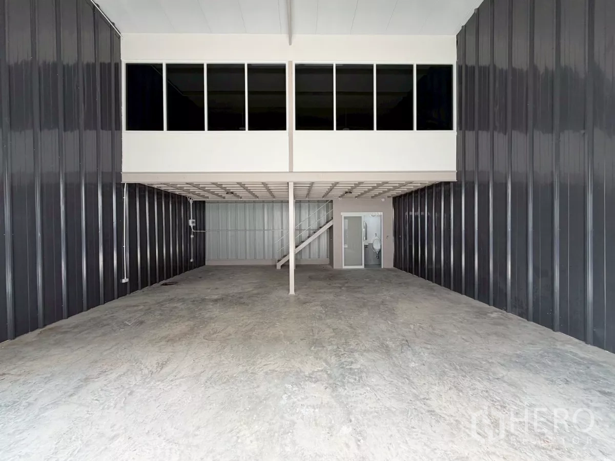 Warehouse for rent in Suan Luang, Bangkok - Spacious warehouse interior with high ceiling, mezzanine office with windows, concrete floor and roller door access.
