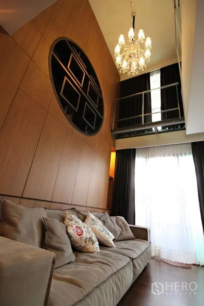 Condominium for rent or sale in Khlong Toei, Bangkok - High-ceiling lounge with chandelier, mezzanine, and large curtained windows.