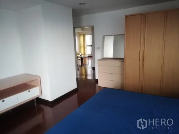 Condominium for rent in Phaya Thai, Bangkok - Primary bedroom with blue bedspread, wooden wardrobe and dresser, and polished hardwood floors leading to the living area.