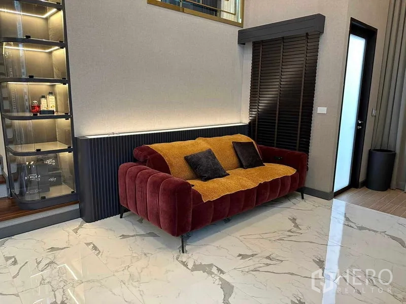 Detached House for sale in Suan Luang, Bangkok - Living area with red velvet sofa, marble-look flooring and illuminated display shelving.