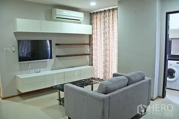 公寓 出租在Phaya Thai, Bangkok - 客厅设壁挂电视柜、空调，并与带洗衣机的厨房相连。