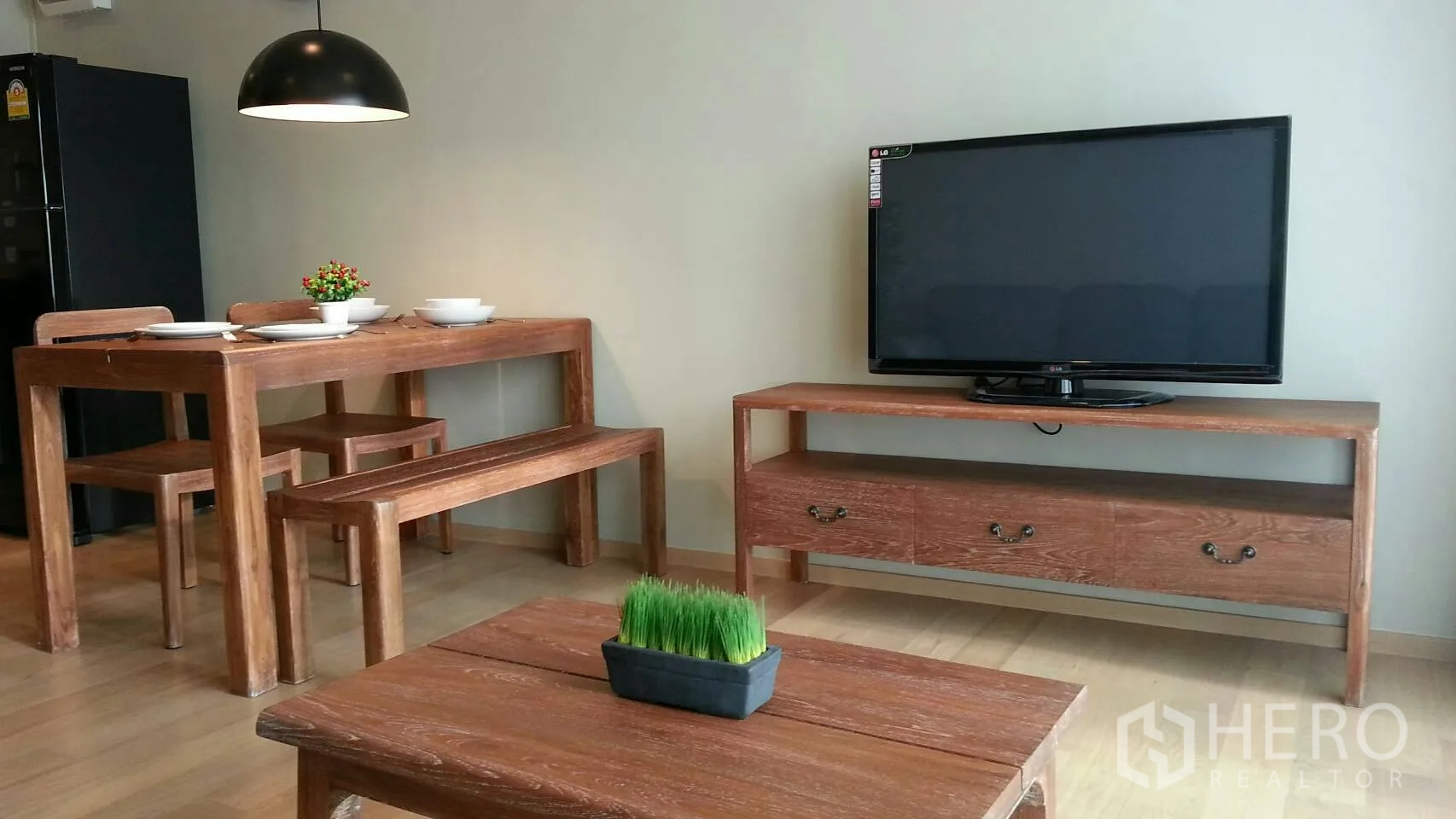 Condominium for rent or sale in Watthana, Bangkok - Open‑plan living and dining area with wooden furniture, flat‑screen TV and light wood flooring.