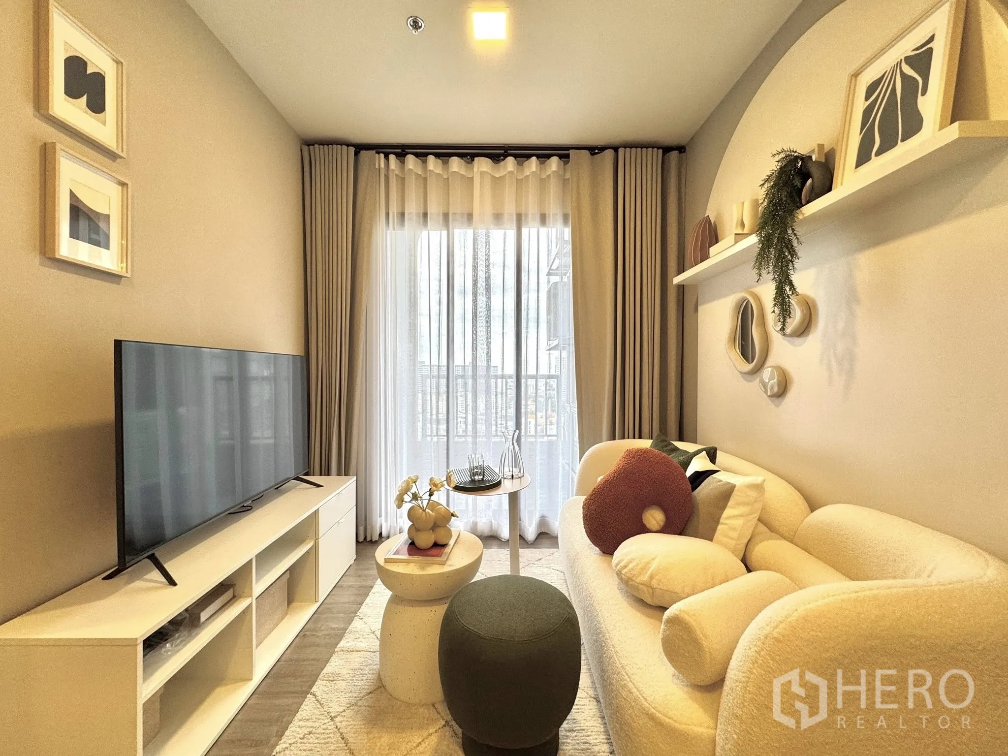 公寓 for rent in Watthana, Bangkok - 客厅设电视柜、奶油色沙发、圆形脚凳与推拉玻璃门。
