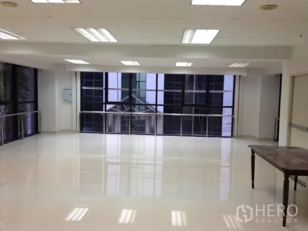 Office Space for rent in Bang Kapi, Bangkok - Spacious office room with wide glass frontage, overhead lighting and a small table in the corner.