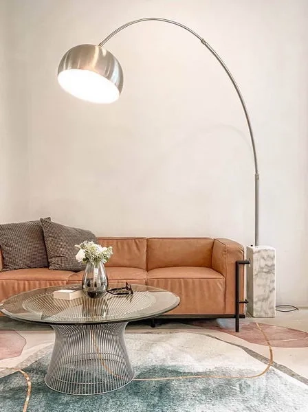 Townhouse for rent in Huai Khwang, Bangkok - Cozy lounge corner with tan leather sofa, arc floor lamp and glass coffee table on a patterned rug.