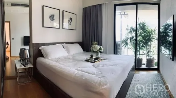 คอนโด ให้เช่าในWatthana, Bangkok - ห้องนอนใหญ่เตียงคิงพร้อมภาพตกแต่ง และประตูกระจกเลื่อนไปยังระเบียงที่มีไม้กระถาง