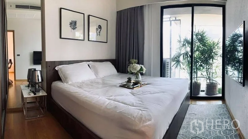 คอนโด ให้เช่าในWatthana, Bangkok - ห้องนอนใหญ่เตียงคิงพร้อมภาพตกแต่ง และประตูกระจกเลื่อนไปยังระเบียงที่มีไม้กระถาง