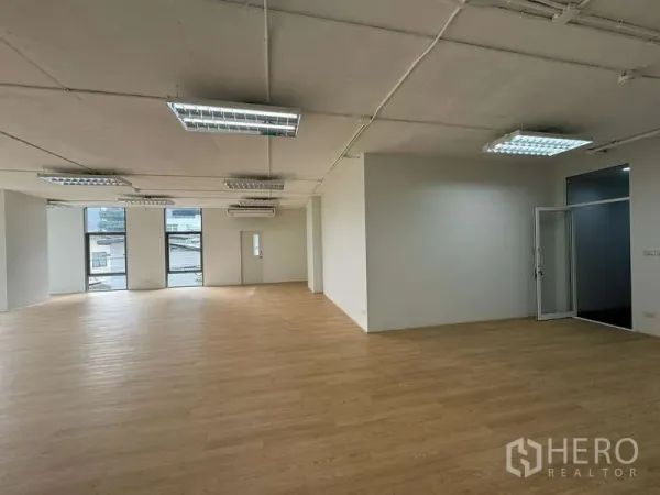 办公空间 出租在Sathon, Bangkok - 开放式办公区，木质地板、白色墙面、荧光灯照明，带玻璃门房间与城市景观窗。