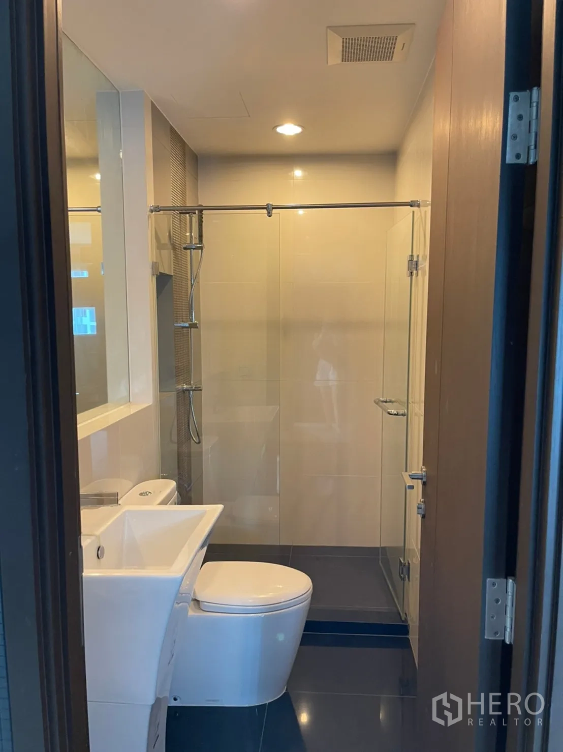 Condominium for sale in Sathon, Bangkok - Modern bathroom with glass-enclosed shower, white basin and toilet.