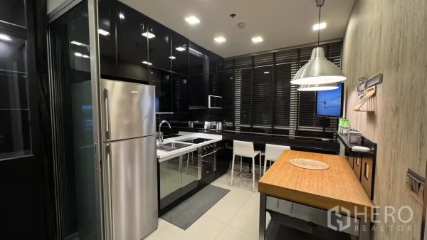 Condominium for rent or sale in Khlong Toei, Bangkok - Modern black-gloss kitchen with stainless refrigerator, double sink, cooktop, and breakfast bar seating.