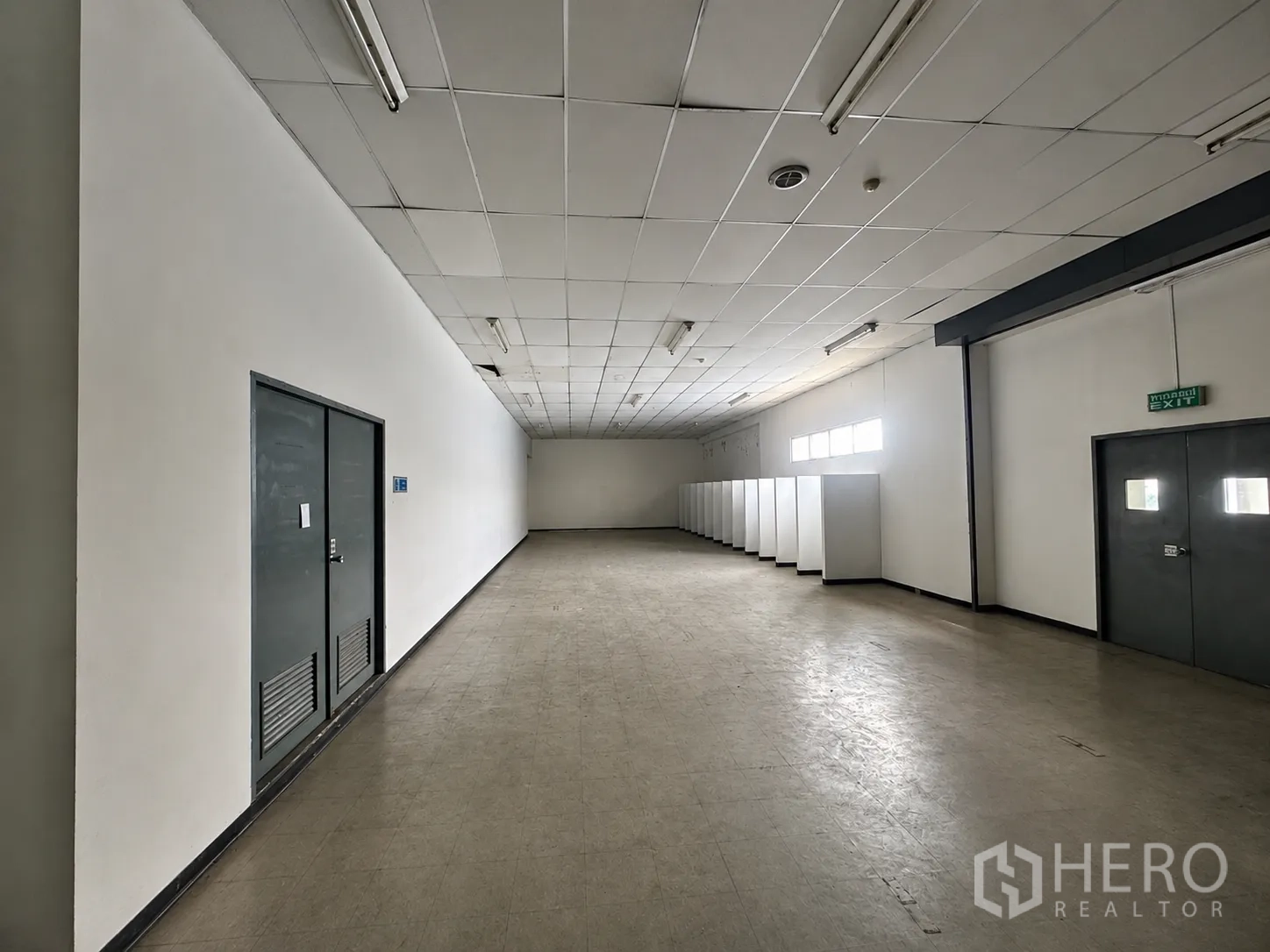 Factory for rent or sale in Wang Noi, Phra Nakhon Si Ayutthaya - Wide interior corridor with high ceiling lights, gray double doors, and a row of white cabinets by the windows.