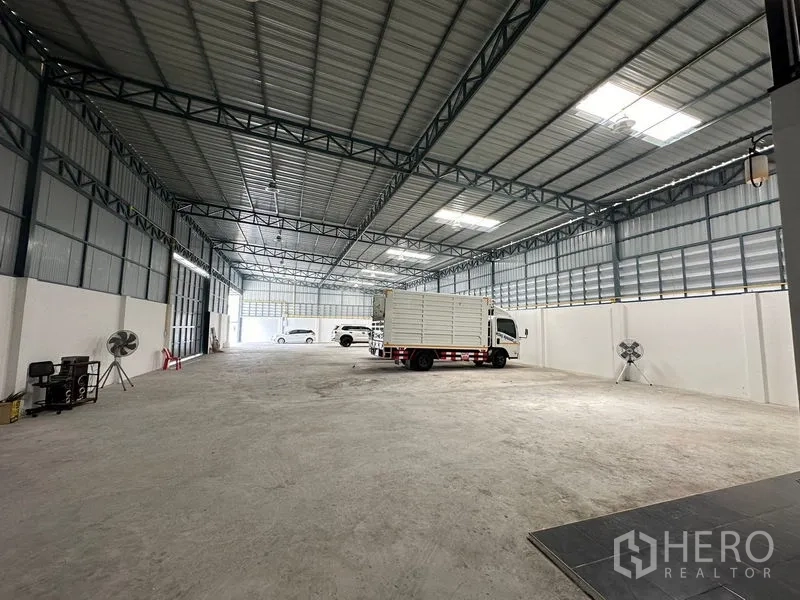 Warehouse for rent in Lam Luk Ka, Pathum Thani - Open warehouse floor with trucks parked under skylights and ventilated metal walls.
