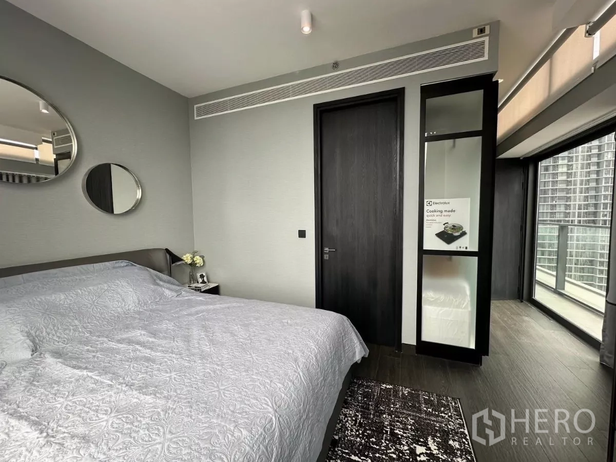 Condominium for rent in Bang Rak, Bangkok - Second bedroom with large bed, mirrors, dark wood door, and access to a glass-walled balcony.