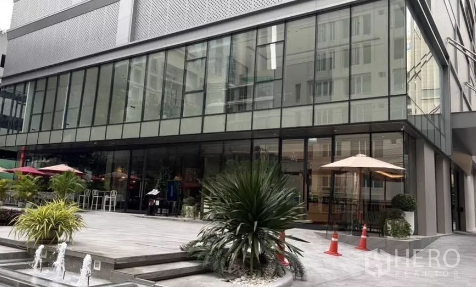 零售空间 出租 - 现代玻璃外立面的商业建筑，带露台遮阳伞、绿植和小喷泉。