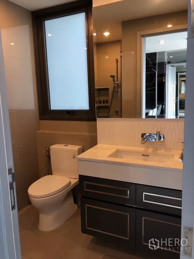 Condominium for rent in Khlong Toei, Bangkok - Modern bathroom featuring window, vanity, toilet and glass-enclosed shower.