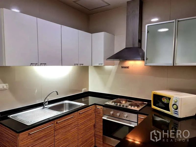 Apartment for rent - Modern L-shaped kitchen with black granite countertop, sink, hob, oven, range hood and white cabinets.