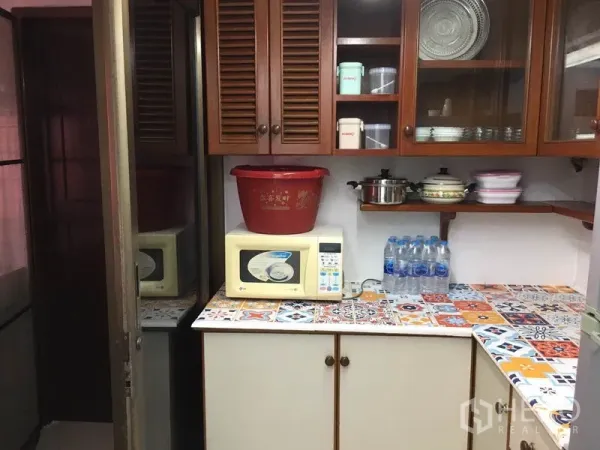 联排别墅 出租在Khlong Toei, Bangkok - 紧凑厨房，木质橱柜、彩色马赛克台面和微波炉。