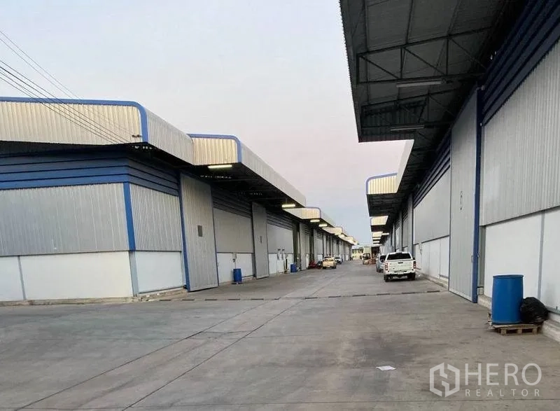 货栈 出租在Lat Krabang, Bangkok - 成排仓库出入口，沿混凝土道路设置雨棚与停靠车辆