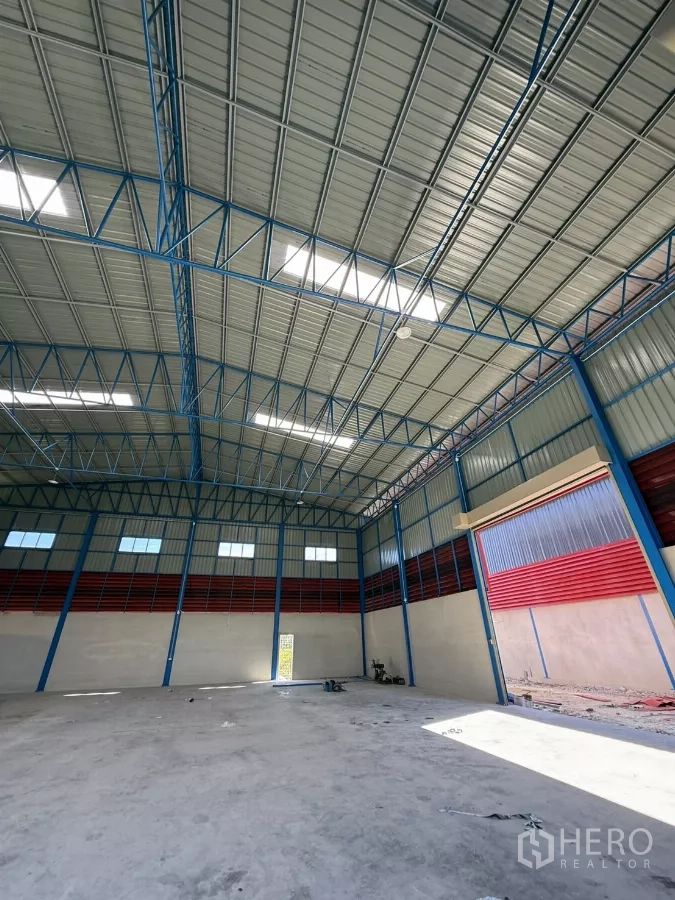 Warehouse for rent in Lam Luk Ka, Pathum Thani - High-roof hall with concrete floor and an open roller door on the right side.