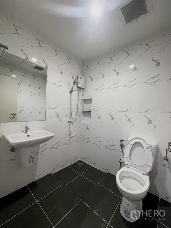 Townhouse for rent in Samut Prakan - Bathroom with white marble-effect tiles, shower, sink and toilet.